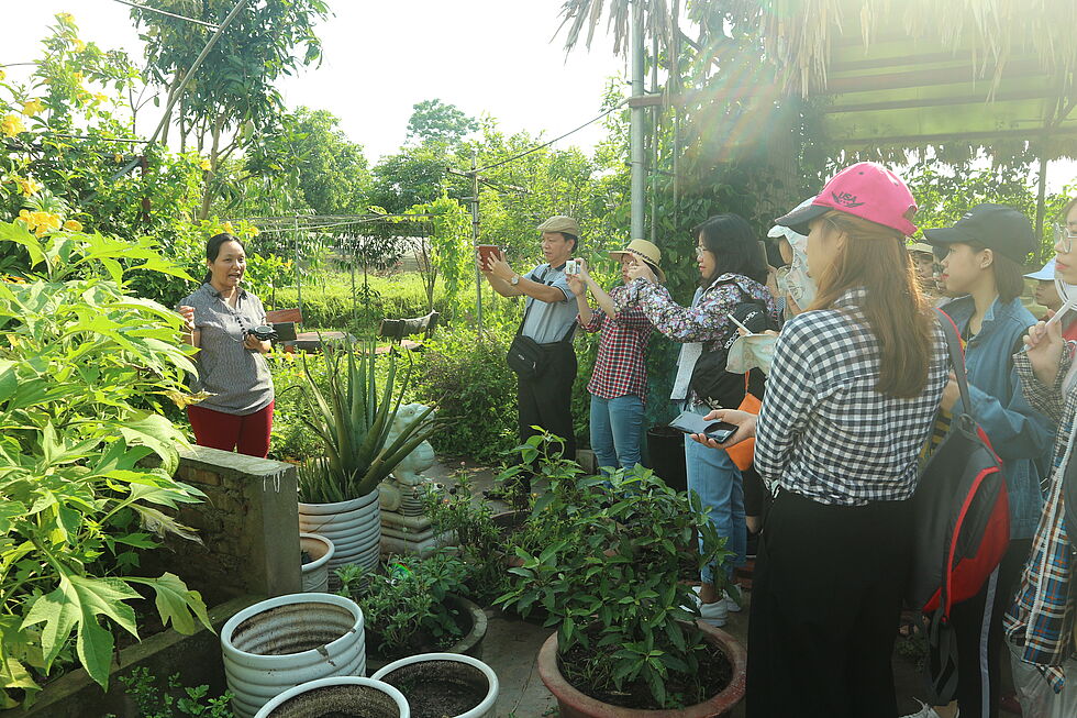 A group of people standing in a farm, a woman sharing about the farm to the others and some people taking photo of her